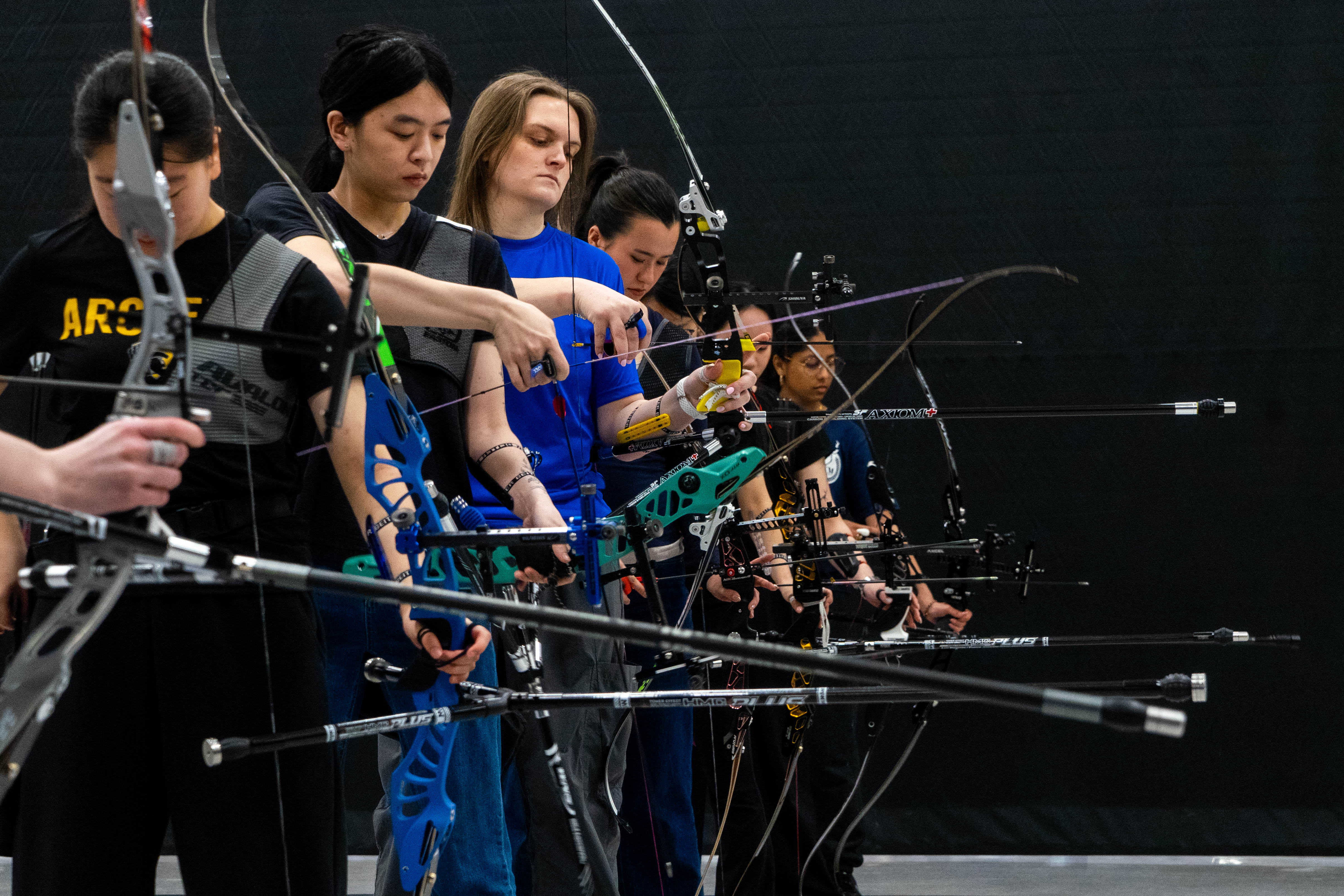 Several archers standing in a row with Olympic Recurve bows at a competition.